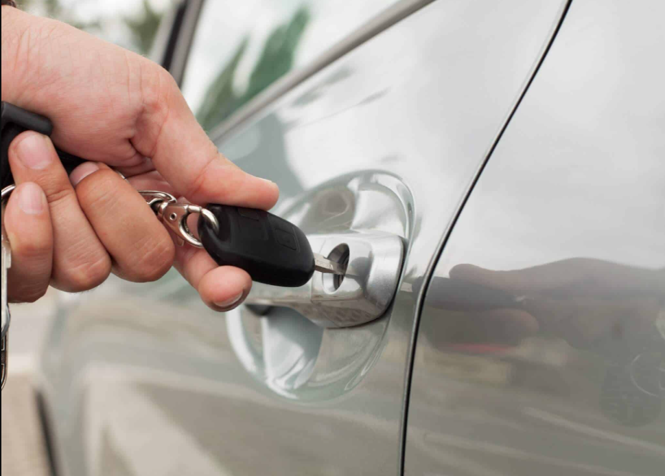 A person inserting a key into a front gray car door and sligtly turning the key.