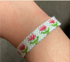 Embroidery bracelet. White bracelet with pink tulips along it on a person's wrist.