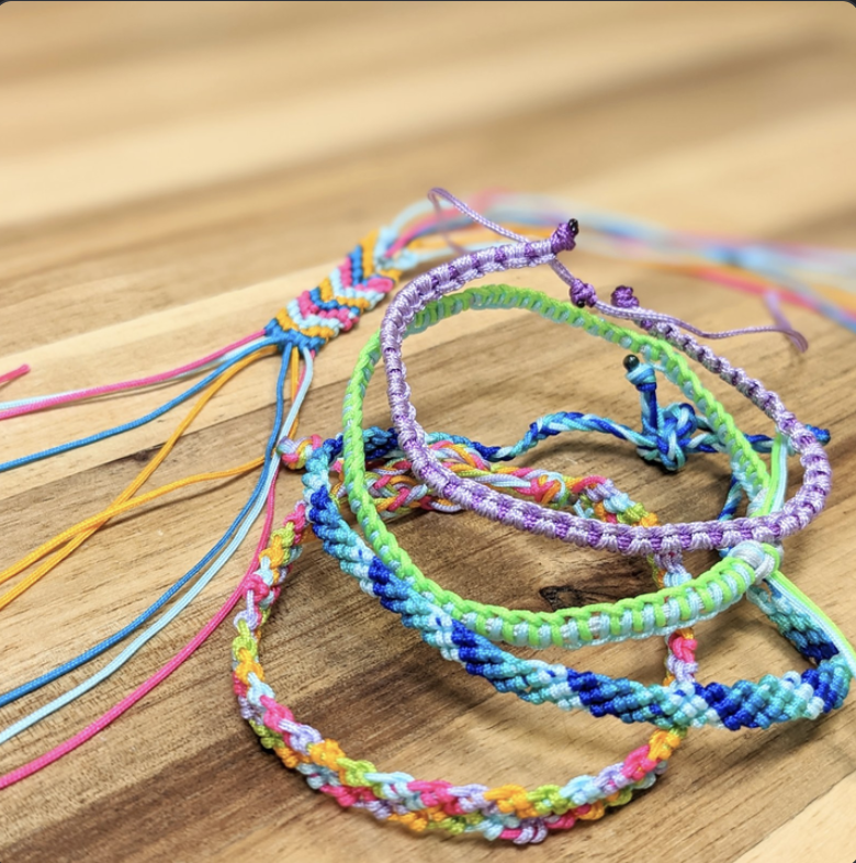 A pile of several embroidery bracelets. They are striped. Some bracelets use shades of blue, green purple, pink, and yellow.
