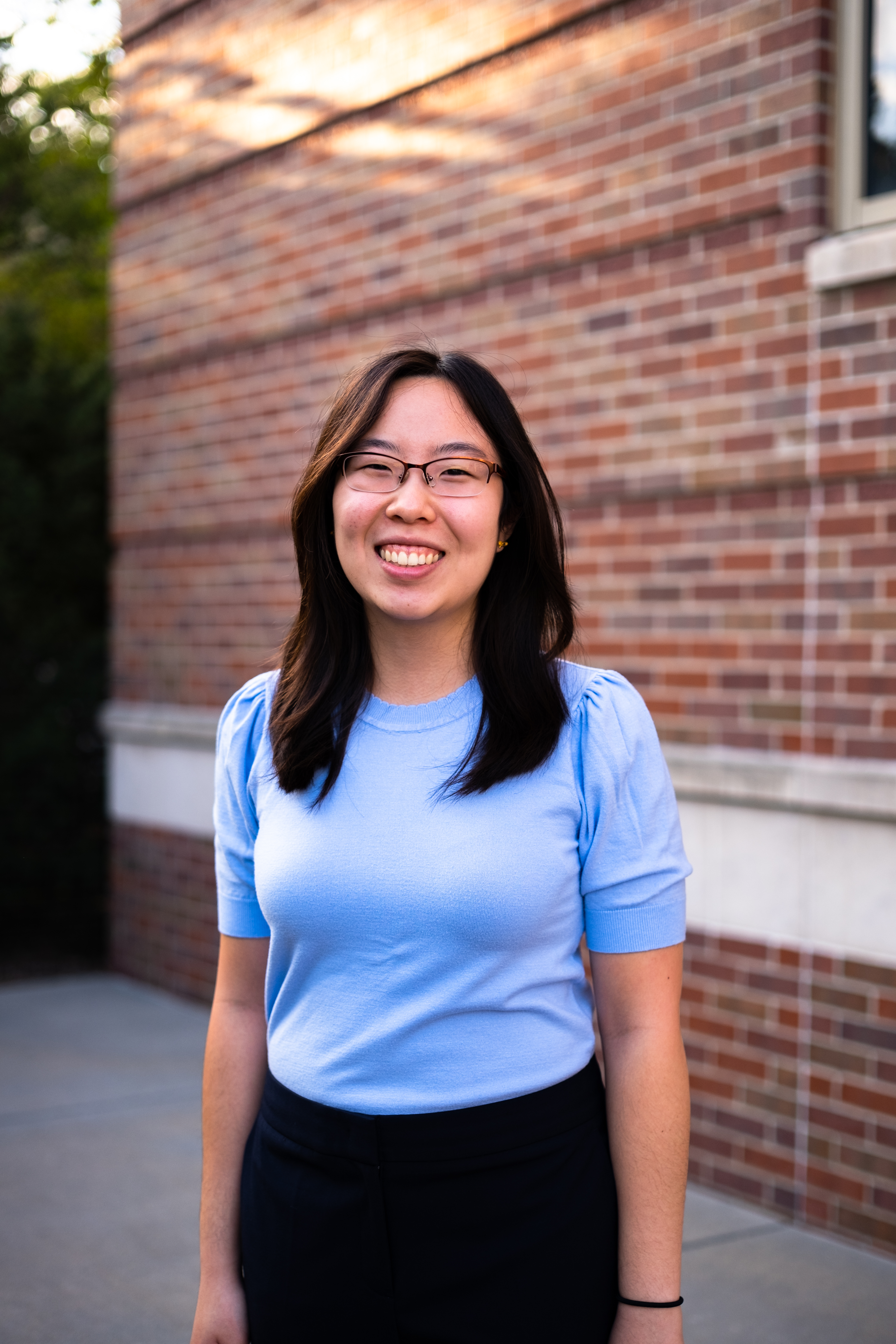 a picture of Victoria Chin. A smiling Asian girl in front of a brick building. She is dressed in business casual.